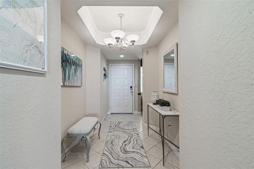 A brightly lit entryway features a tiled floor, a runner rug, and a tray ceiling — 4953 BACOPA LANE S UNIT 204, ST PETERSBURG, FL