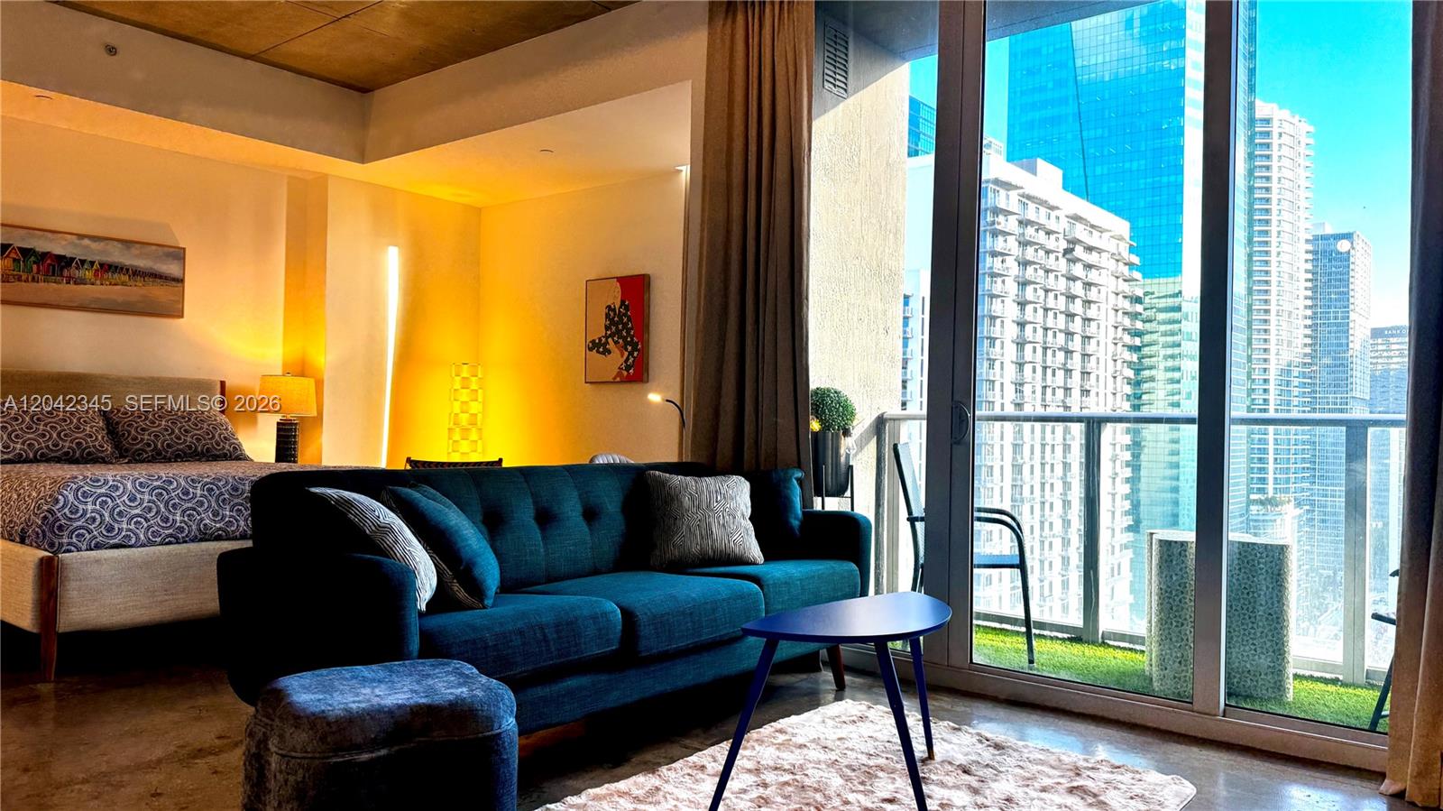 A modern living room with a blue sofa and bed overlooks a city skyline — 151 SE 1st St # 2205, Miami FL 33131, MIAMI, FL