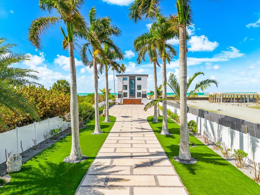 A paved driveway leads toward a modern house framed by palm trees near the ocean — 811 N SHORE DRIVE, ANNA MARIA, FL