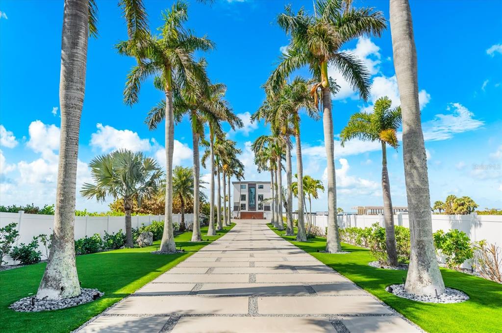 A long paved driveway lined with tall palm trees leads to a modern multi-story house — 811 N SHORE DRIVE, ANNA MARIA, FL