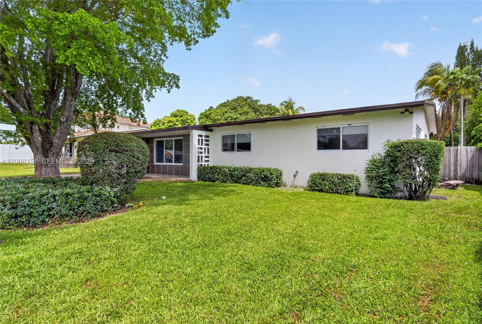 A single-story white house with a flat roof sits behind a green lawn and bushes — 1155 NE 184th St, Miami FL 33179, MIAMI, FL