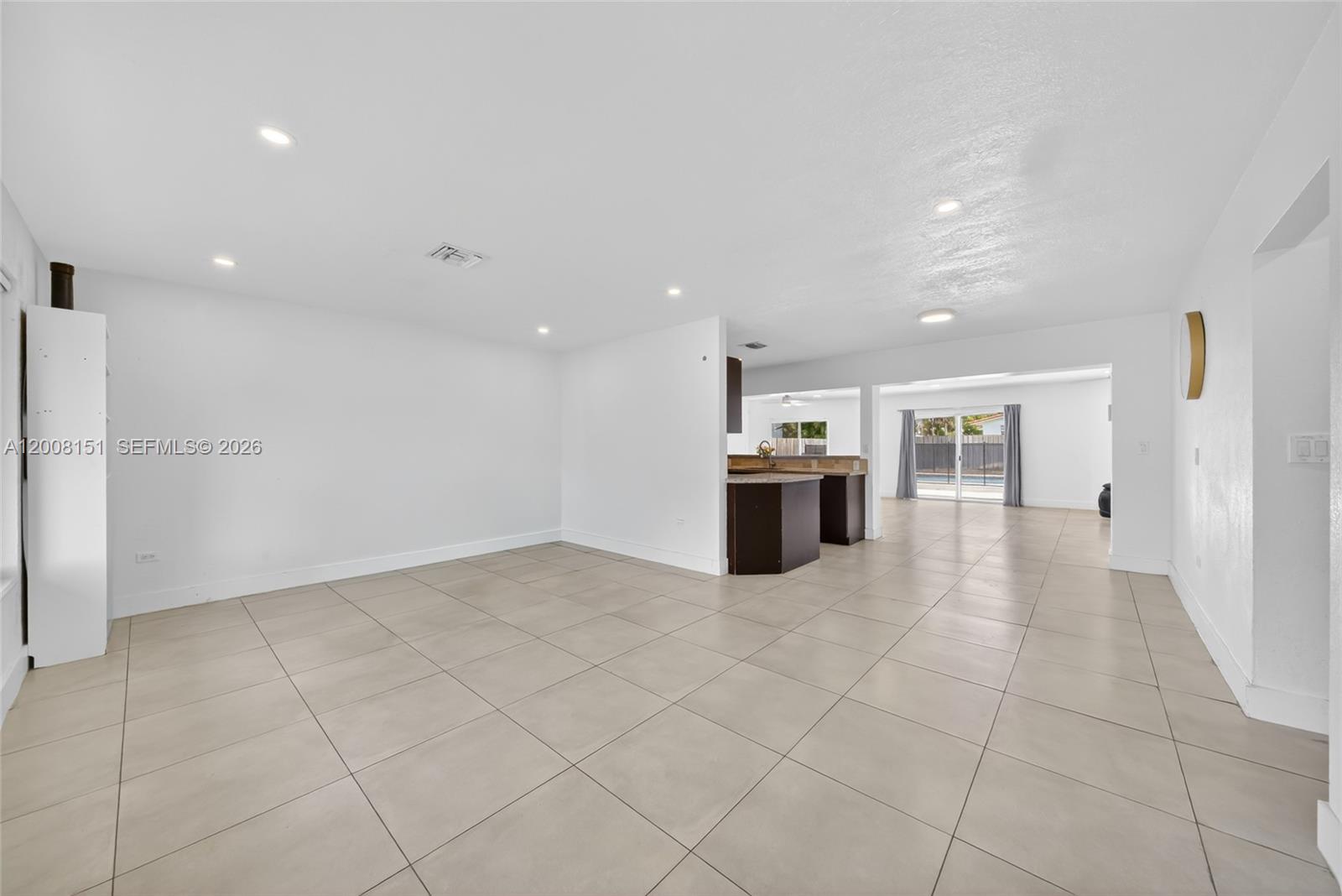 An open-concept living area features light-colored tile flooring and a view into the kitchen — 1155 NE 184th St, Miami FL 33179, MIAMI, FL