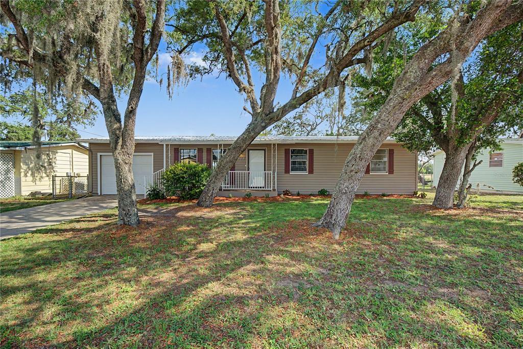 A single-story house with tan siding and a metal roof sits behind several large trees — 4717 HOWARD STREET, SEBRING, FL