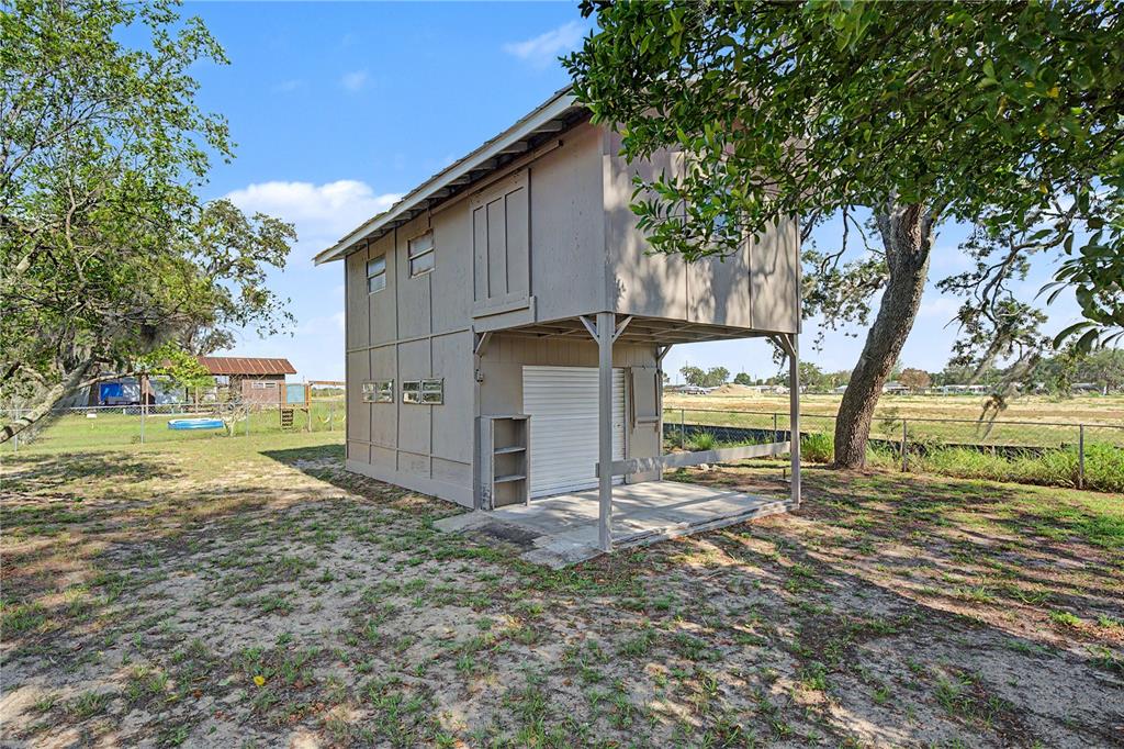 A two-story wooden shed with a roll-up garage door and an open-air ground level patio — 4717 HOWARD STREET, SEBRING, FL