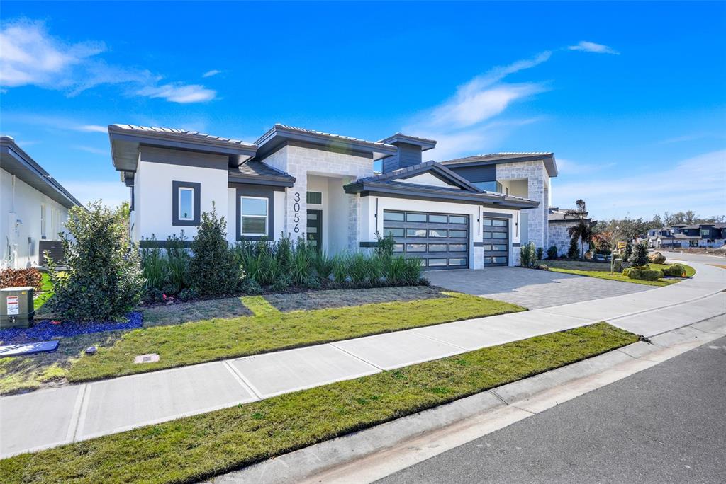 A modern single-story house with a white stone facade, dark trim, and a three-car garage — 3056 KENSINGTON AVENUE, DAVENPORT, FL
