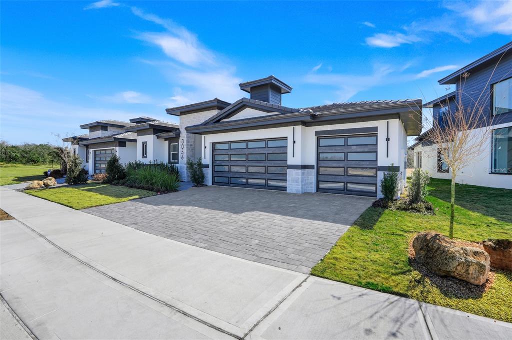 A modern single-story house exterior features a paved driveway, two garage doors, and stone accents — 3056 KENSINGTON AVENUE, DAVENPORT, FL