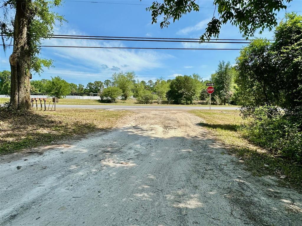 A dirt driveway leads toward a paved road with a stop sign and trees — 12100 NW US HIGHWAY 441, ALACHUA, FL