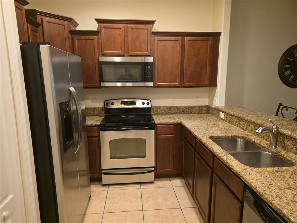 A kitchen features wood cabinets, granite countertops, stainless steel appliances, and tile flooring — 3158 RODRICK CIRCLE UNIT 3158, ORLANDO, FL