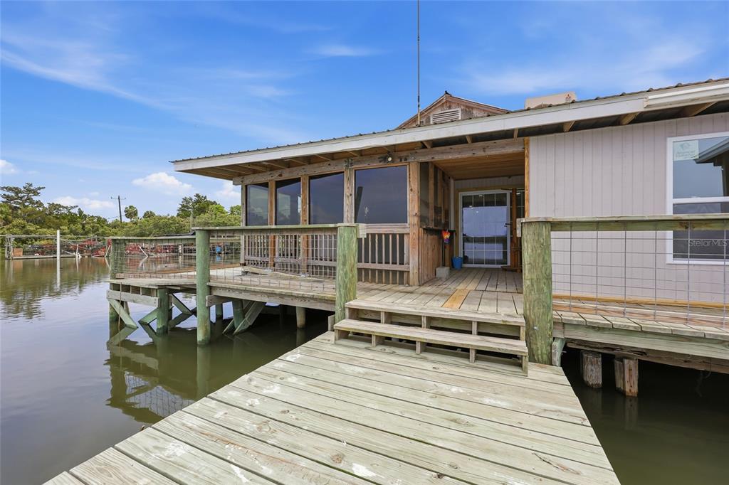 A wooden deck leads to a screened-in porch and entrance of a house over water — 505 3RD STREET, CEDAR KEY, FL
