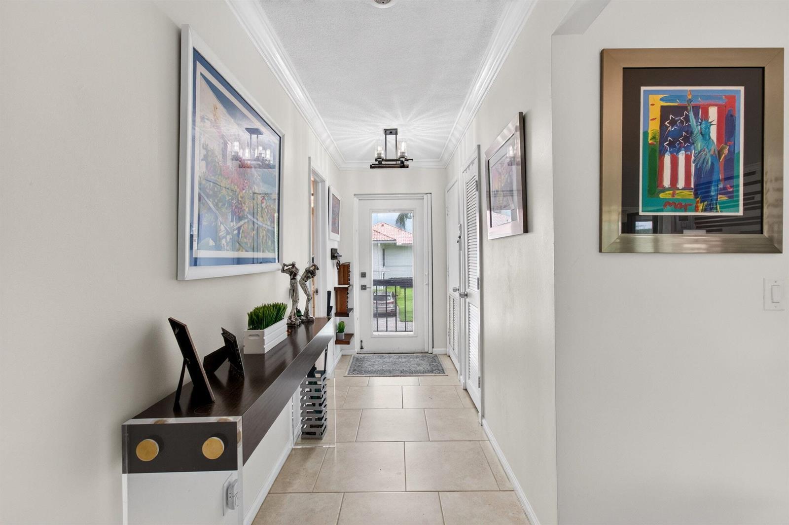 A hallway with tile floors, a floating console table, and framed art leads to a door — 4084 N Quail Ridge Drive Unit B, Boynton Beach FL 33436, BOYNTON BEACH, FL