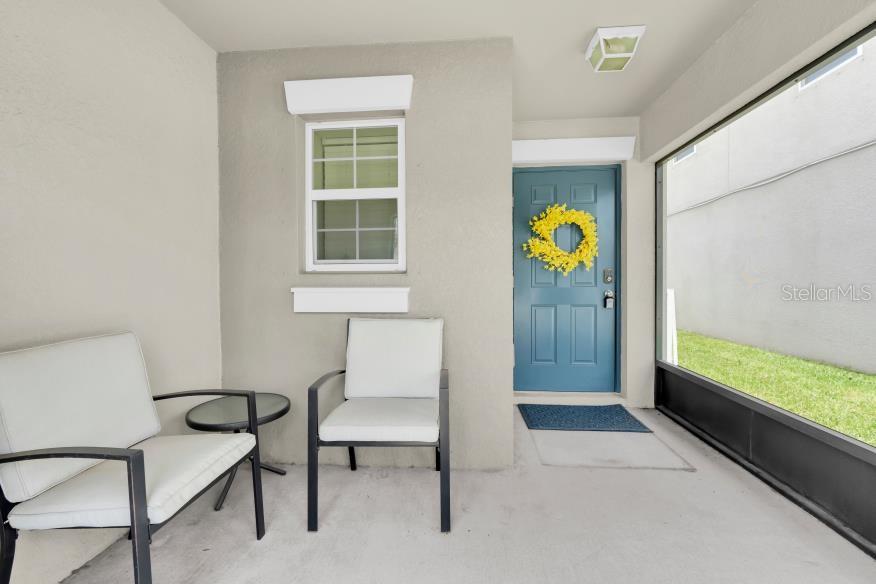 A covered patio features two chairs, a small table, a window, and a blue front door — 17010 YELLOW PINE STREET, WIMAUMA, FL