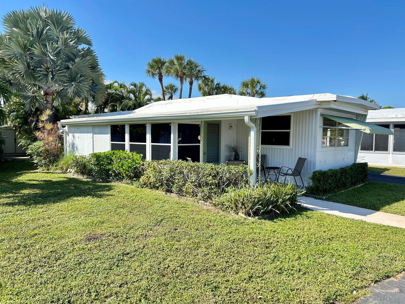 A white mobile home features a screened-in porch, palm trees, and a manicured lawn — 425 E Bougainvillea Drive, Deerfield Beach FL 33442, DEERFIELD BEACH, FL