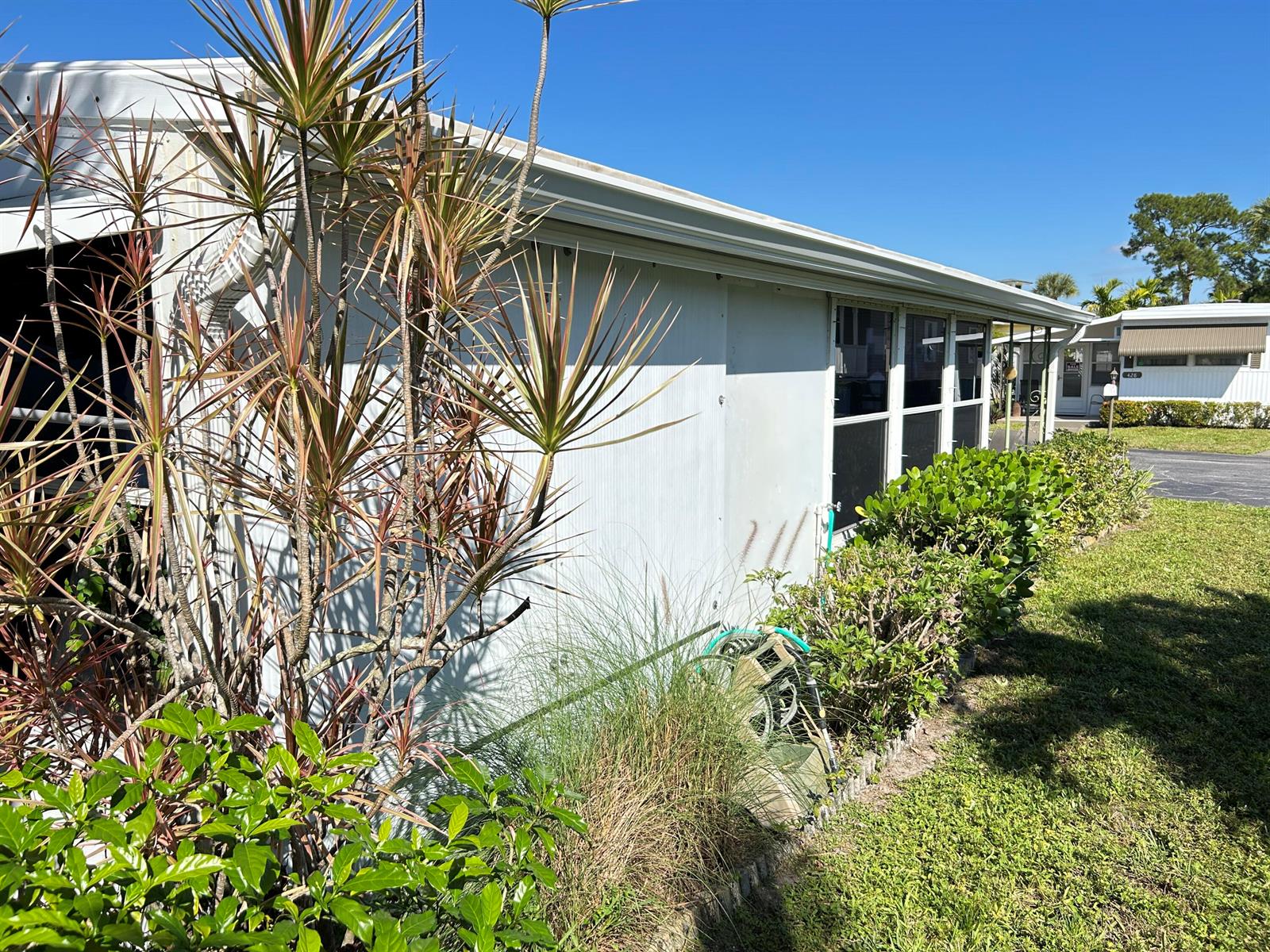The exterior of a mobile home features light-colored siding, a screened window, and landscaping — 425 E Bougainvillea Drive, Deerfield Beach FL 33442, DEERFIELD BEACH, FL