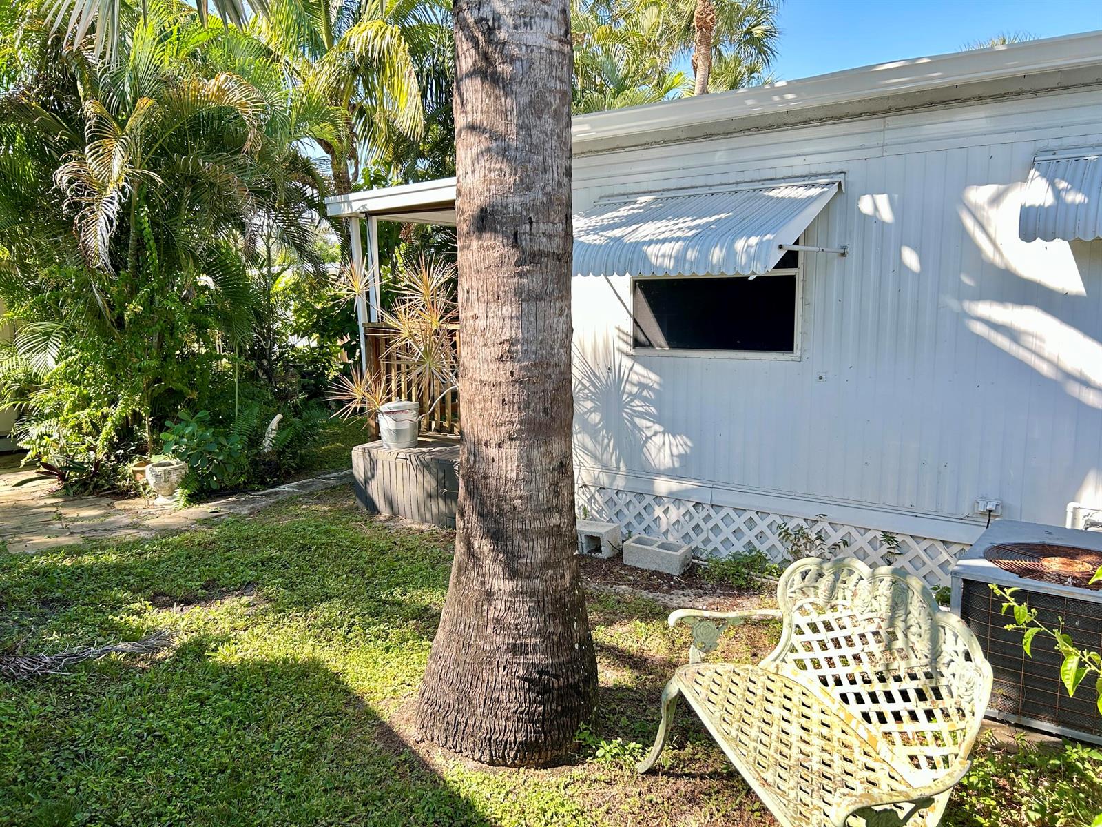 A palm tree stands in a yard next to a white mobile home with an awning — 425 E Bougainvillea Drive, Deerfield Beach FL 33442, DEERFIELD BEACH, FL