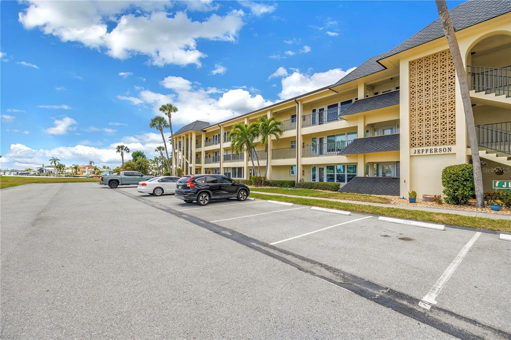 A three-story apartment building with a parking lot in the foreground under a blue sky — 4700 COVE CIRCLE UNIT 103, ST PETERSBURG, FL