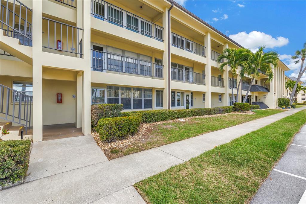 A multi-story apartment building exterior features balconies, a concrete walkway, and manicured landscaping — 4700 COVE CIRCLE UNIT 103, ST PETERSBURG, FL