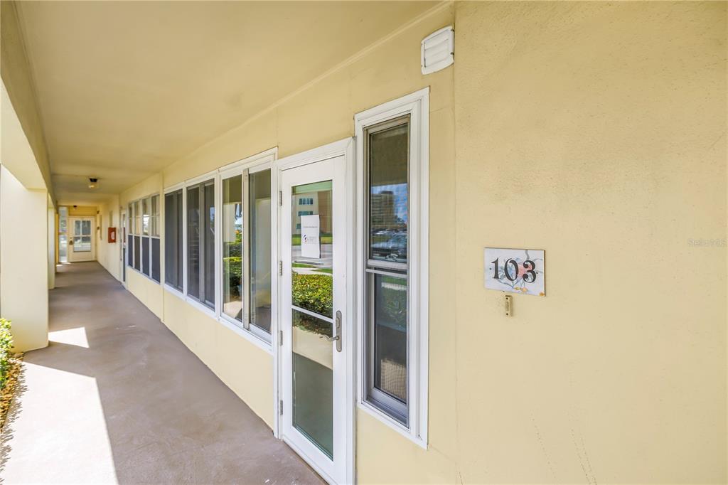 An exterior view of a building walkway with a glass door labeled 103 — 4700 COVE CIRCLE UNIT 103, ST PETERSBURG, FL