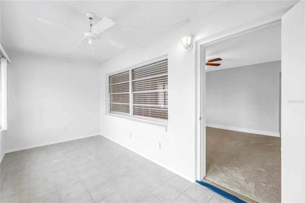 A sunroom with white walls, tile flooring, a ceiling fan, and a doorway to another room — 4700 COVE CIRCLE UNIT 103, ST PETERSBURG, FL