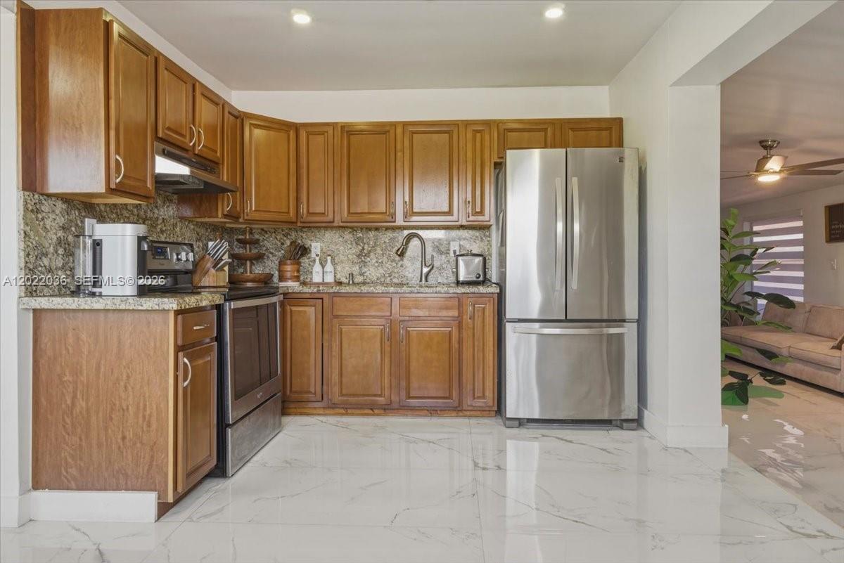 A kitchen features wood cabinets, granite countertops, stainless steel appliances, and white tile flooring — 120 W 50th St, Hialeah FL 33012, HIALEAH, FL
