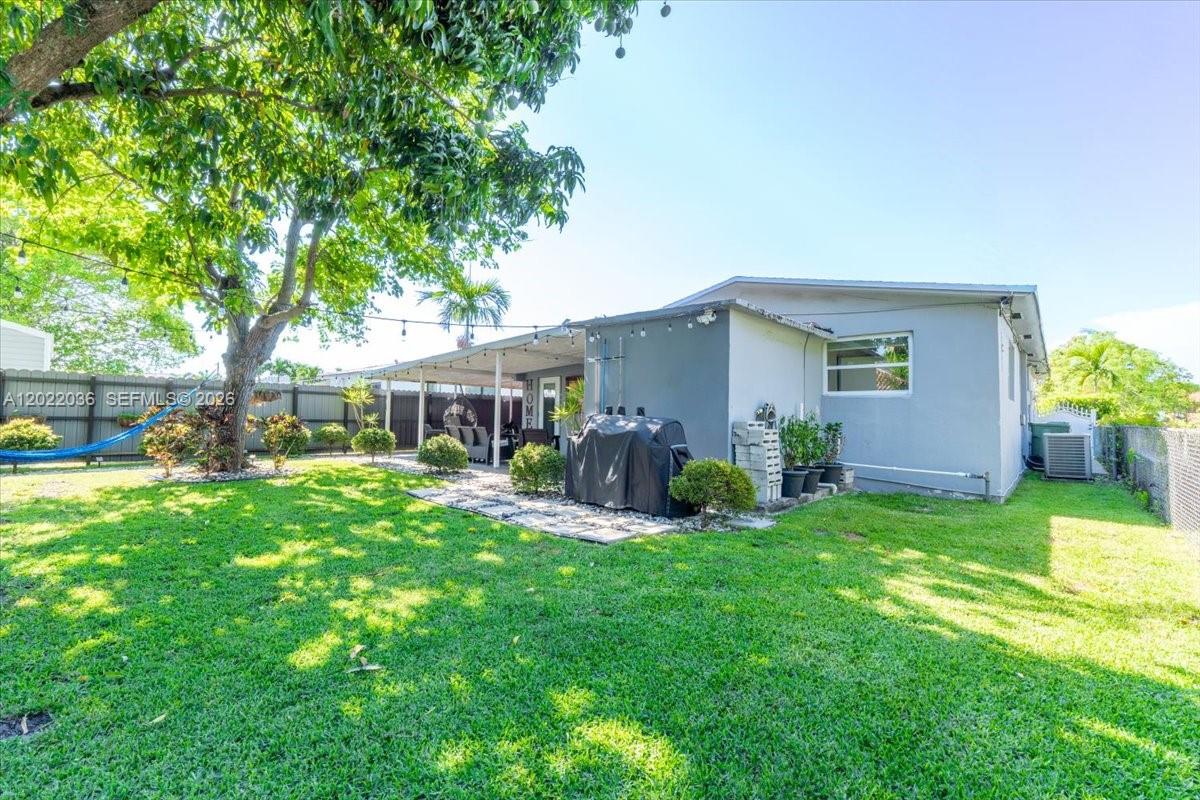 A backyard features a grassy lawn, a covered patio, and a large tree — 120 W 50th St, Hialeah FL 33012, HIALEAH, FL