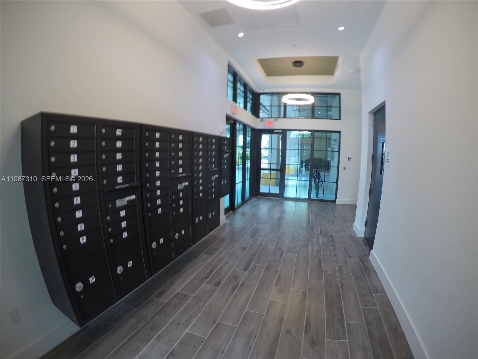 A modern mailroom features dark metal mailboxes, wood-look tile flooring, and glass-paned exterior doors — 4100 SW 64th Ave # 409, Davie FL 33314, DAVIE, FL