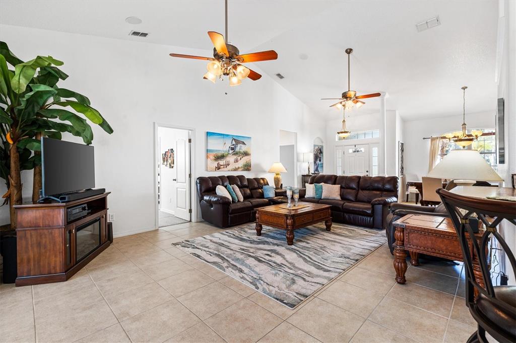 A spacious living room features tile flooring, vaulted ceilings, two ceiling fans, and leather furniture — 12107 EAGLE POINT COURT, LEESBURG, FL