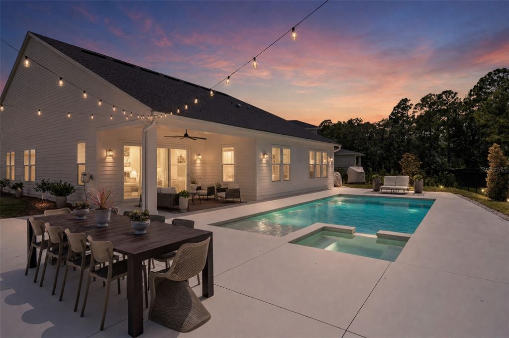 A white house with a covered patio, outdoor dining set, and a swimming pool at dusk — 3135 VANGUARD COURT, ST CLOUD, FL