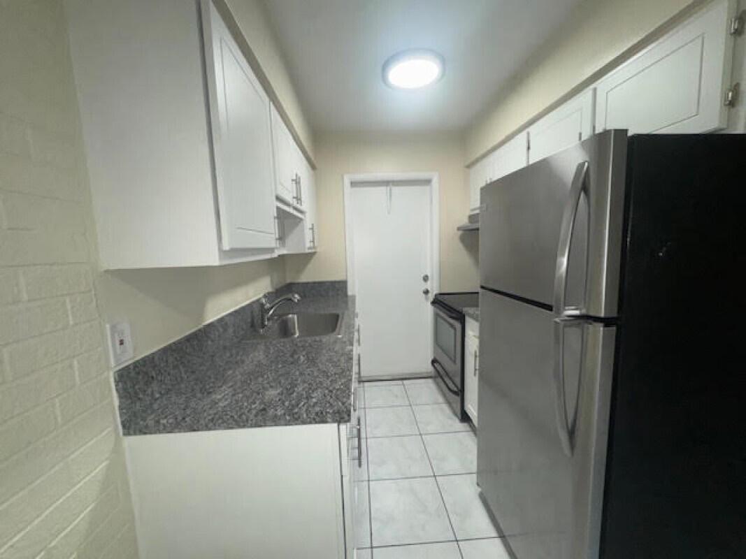 A galley kitchen features white cabinets, granite countertops, stainless steel appliances, and white tile flooring — 1751 NE 31st Street # 26, Pompano Beach FL 33064, POMPANO BEACH, FL