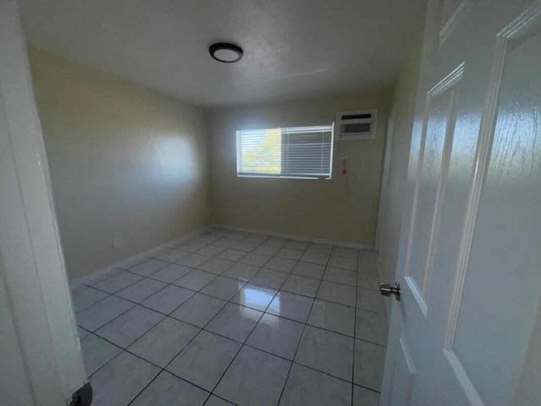 An empty bedroom features light-colored tile flooring, a window with blinds, and a ceiling light — 1751 NE 31st Street # 26, Pompano Beach FL 33064, POMPANO BEACH, FL