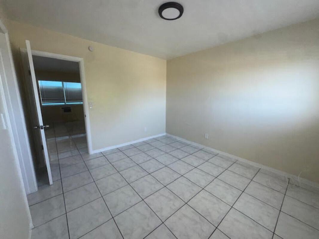 An empty room with beige walls, white tile flooring, and an open doorway — 1751 NE 31st Street # 26, Pompano Beach FL 33064, POMPANO BEACH, FL