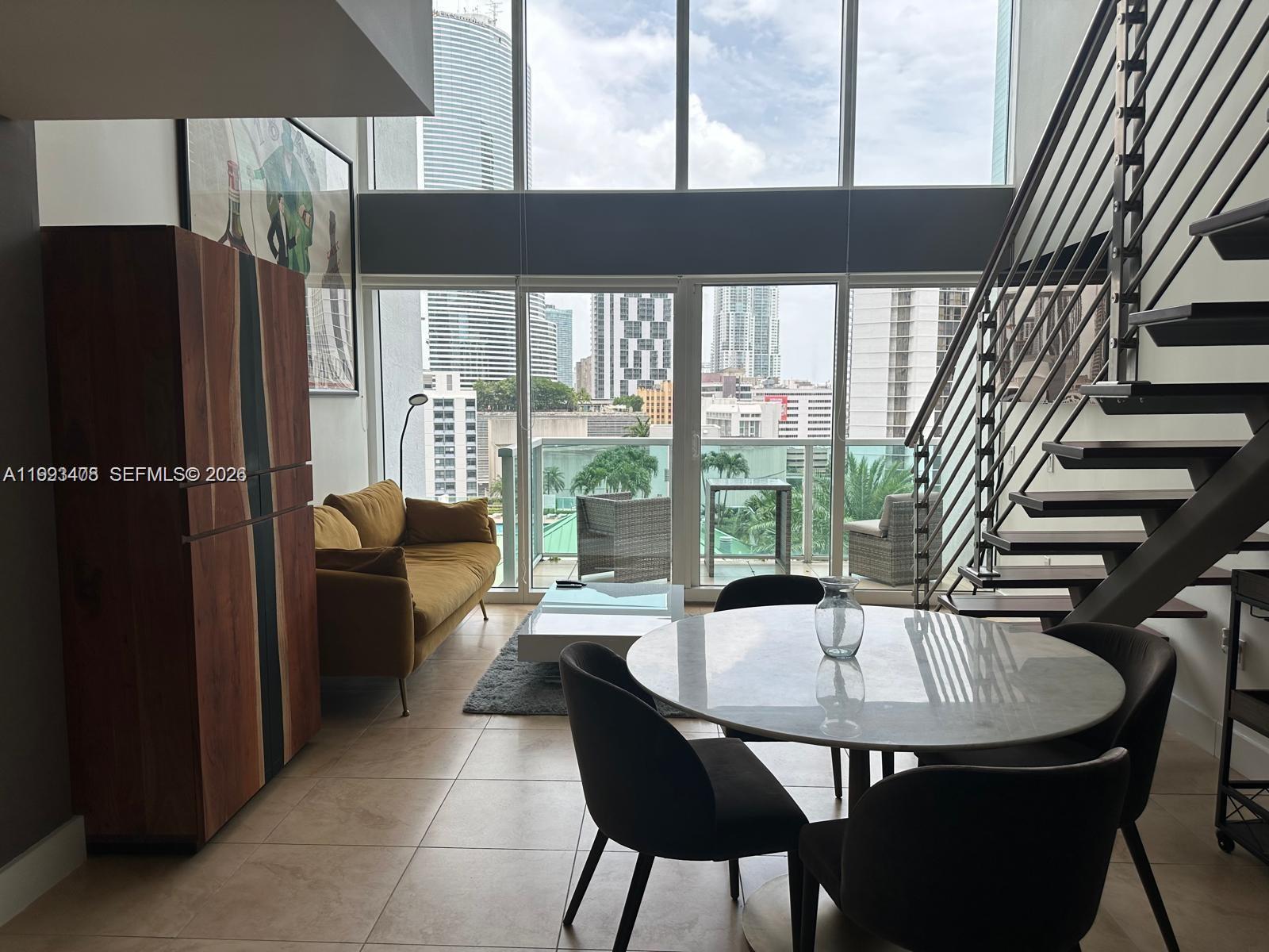 A modern living and dining area features floor-to-ceiling windows, a staircase, and city views — 41 SE 5th St # 903, Miami FL 33131, MIAMI, FL