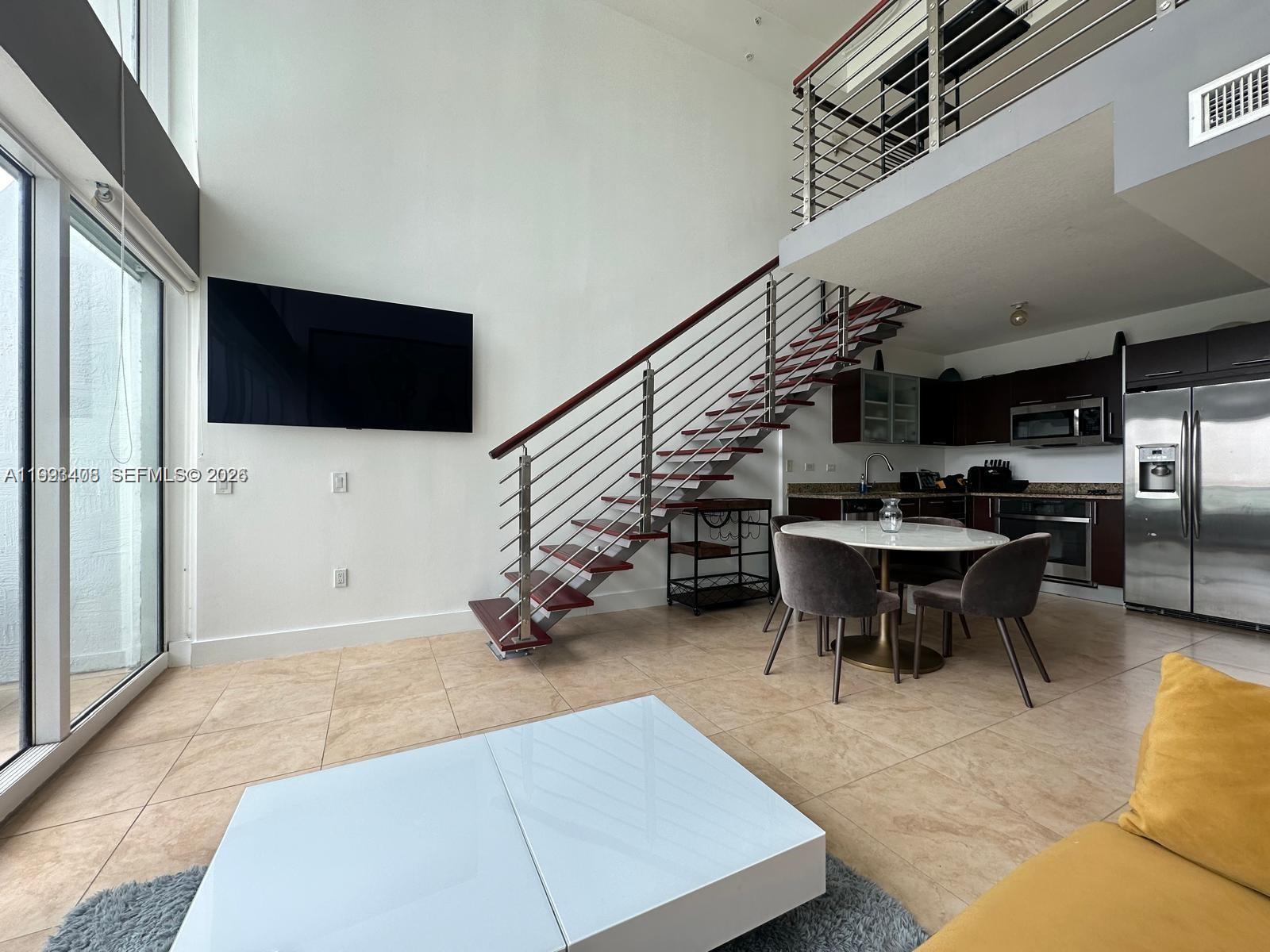 A modern living and dining area features a floating staircase, high ceilings, and tile floors — 41 SE 5th St # 903, Miami FL 33131, MIAMI, FL