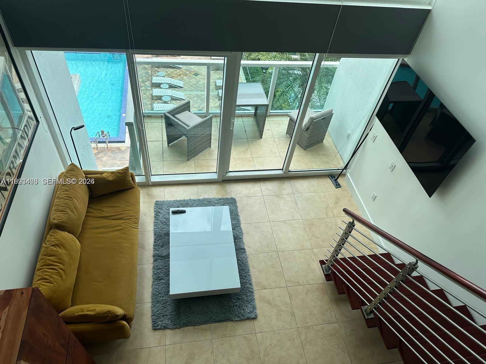 A high-angle view of a living room with a yellow sofa, balcony, and staircase — 41 SE 5th St # 903, Miami FL 33131, MIAMI, FL