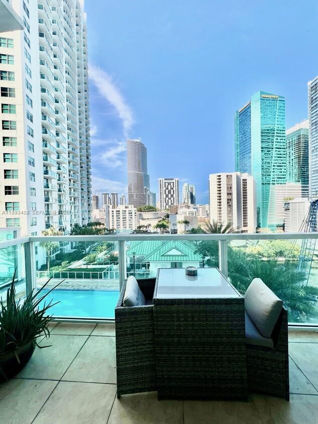 A balcony with a small table and chairs overlooks a swimming pool and city skyline — 41 SE 5th St # 903, Miami FL 33131, MIAMI, FL