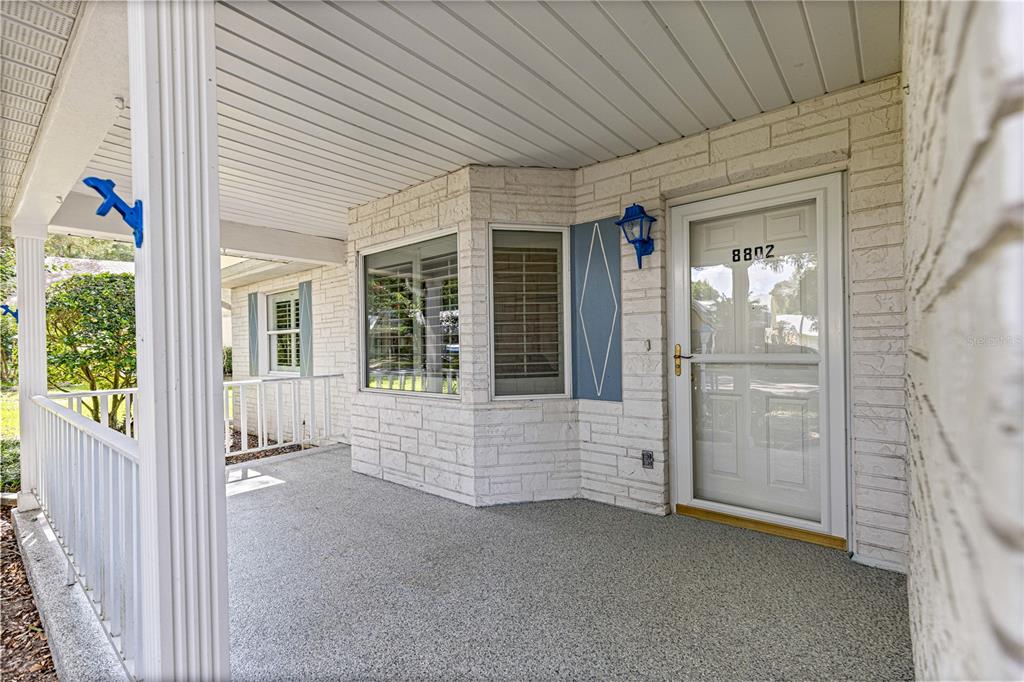 A covered porch features a white brick exterior, a gray textured floor, and a front door — 8802 SW 92ND STREET UNIT A, OCALA, FL