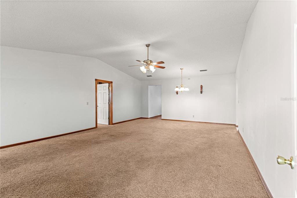 An empty living room features beige carpeting, white walls, a ceiling fan, and a chandelier — 8802 SW 92ND STREET UNIT A, OCALA, FL