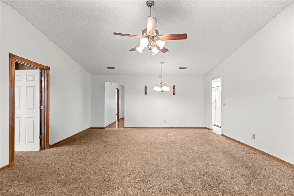 A carpeted room features a ceiling fan, a chandelier, and doorways leading to other areas — 8802 SW 92ND STREET UNIT A, OCALA, FL