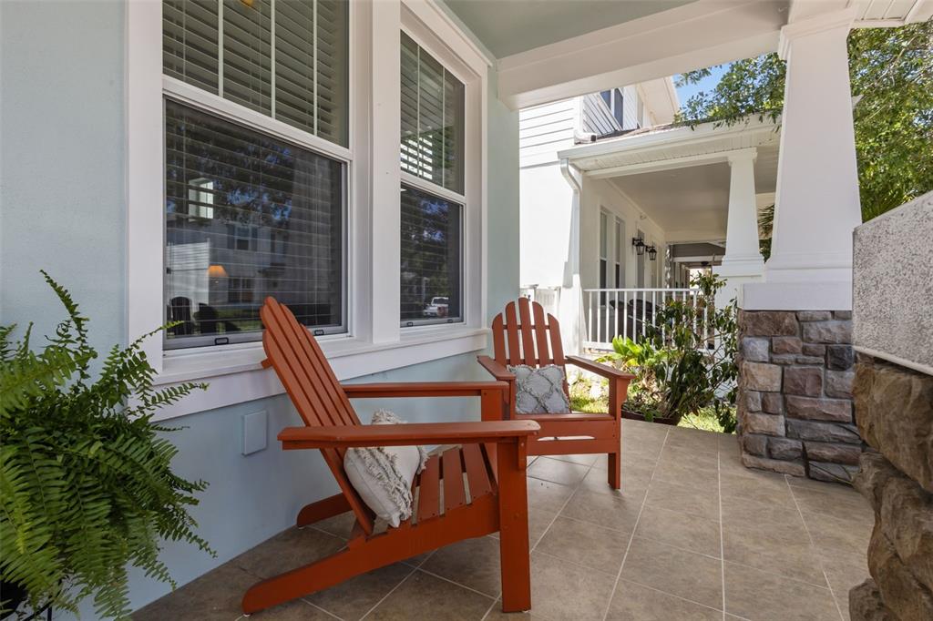 Two orange Adirondack chairs sit on a tiled front porch with stone pillar accents — 3537 PICKERELL PLACE, NEW PORT RICHEY, FL