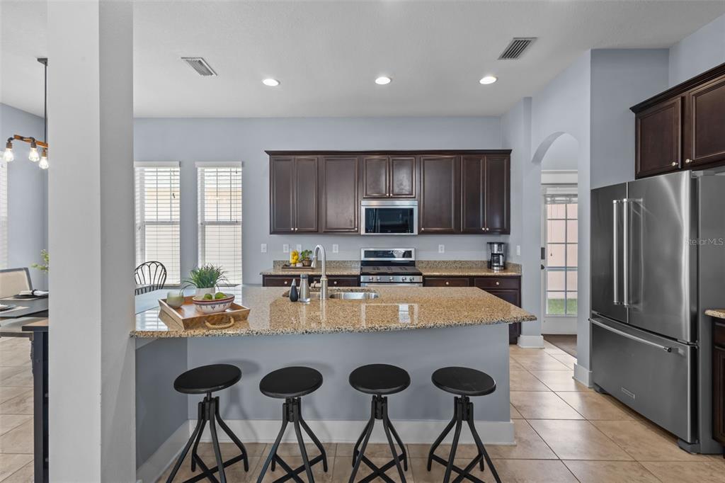 A kitchen features dark wood cabinets, granite countertops, a breakfast bar, and stainless steel appliances — 3537 PICKERELL PLACE, NEW PORT RICHEY, FL