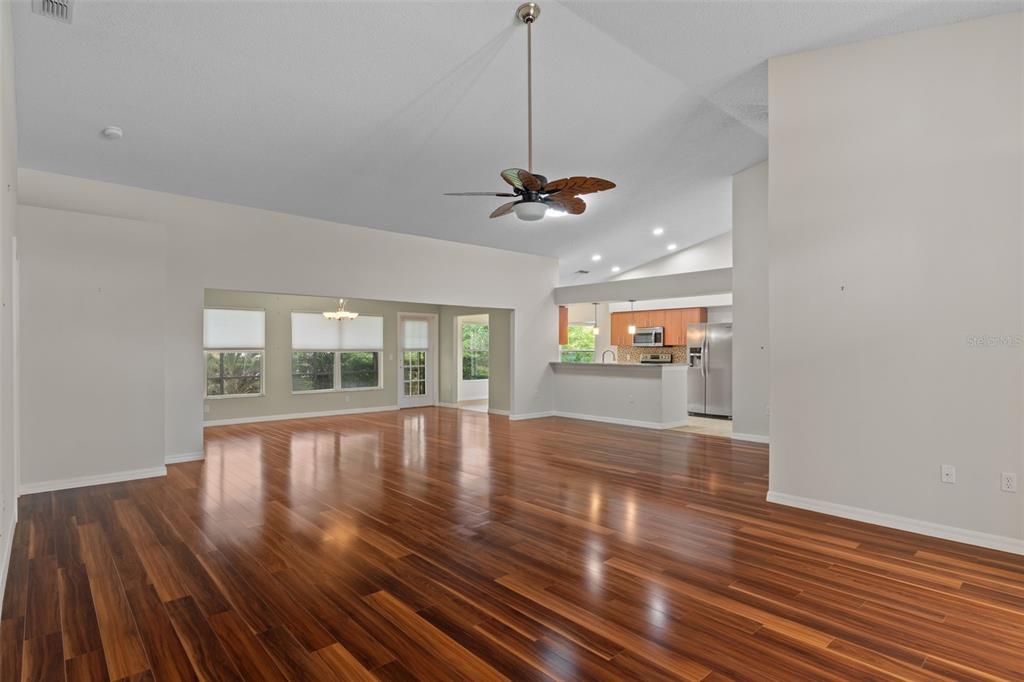 A spacious living area with dark wood flooring, a ceiling fan, and an open kitchen — 18055 TARRINGTON PLACE, HUDSON, FL