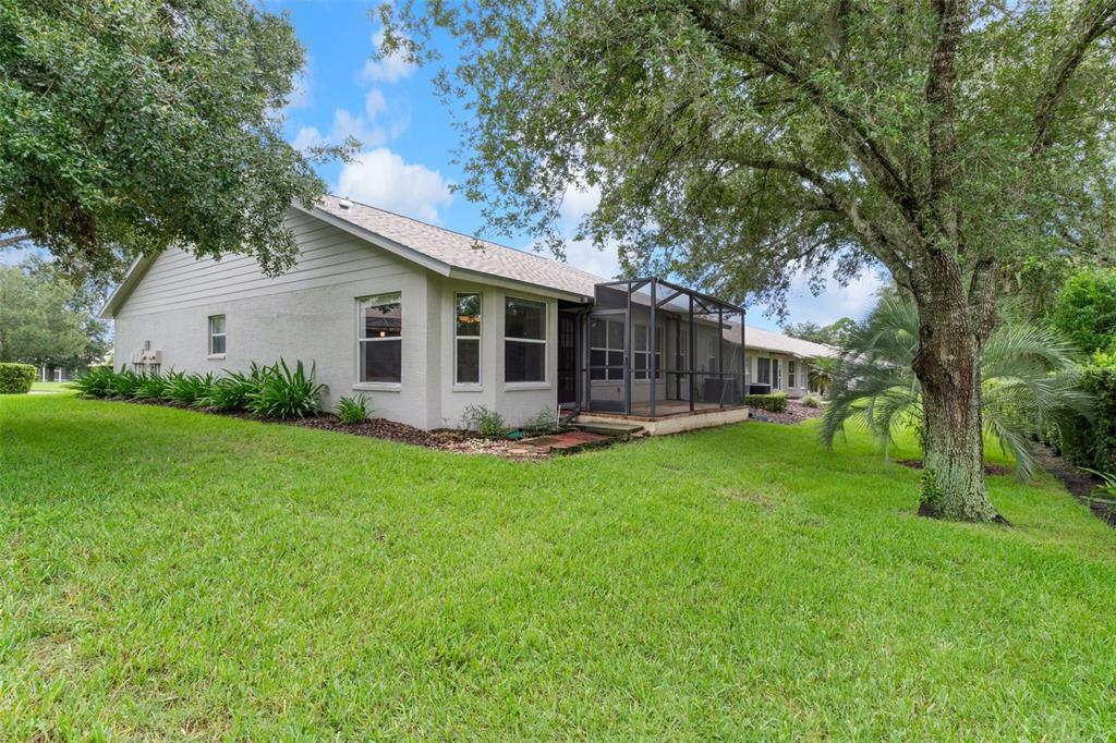 The exterior of a single-story house featuring a screened-in patio and a large grassy yard — 18055 TARRINGTON PLACE, HUDSON, FL