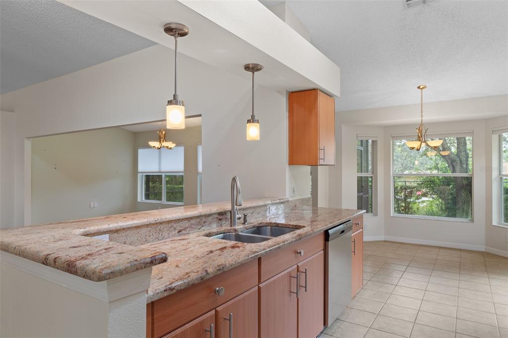 A kitchen with granite countertops, wood cabinets, stainless steel sink, and an adjacent dining area — 18055 TARRINGTON PLACE, HUDSON, FL
