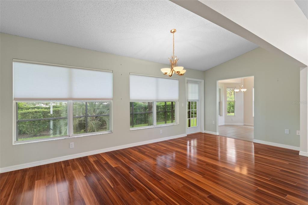 An empty room with hardwood floors, a vaulted ceiling, a chandelier, and large windows — 18055 TARRINGTON PLACE, HUDSON, FL