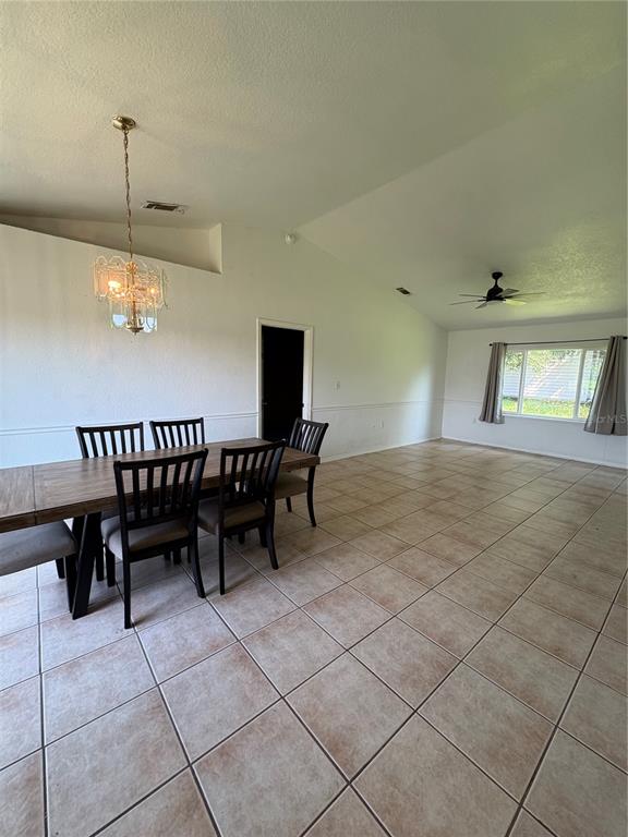 A dining area with a wood table, chairs, chandelier, and tile flooring under a vaulted ceiling — 2302 BELEN DRIVE, DELTONA, FL