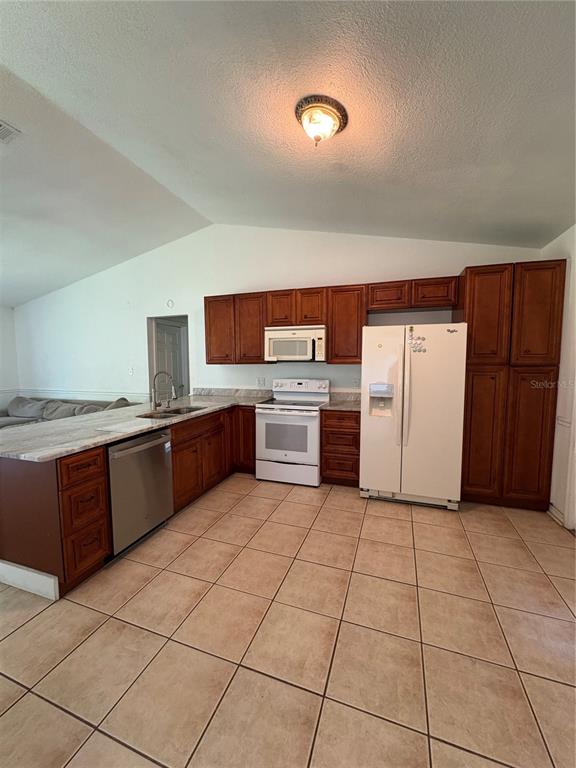 A kitchen features wood cabinets, white appliances, a stainless steel dishwasher, and tile flooring — 2302 BELEN DRIVE, DELTONA, FL