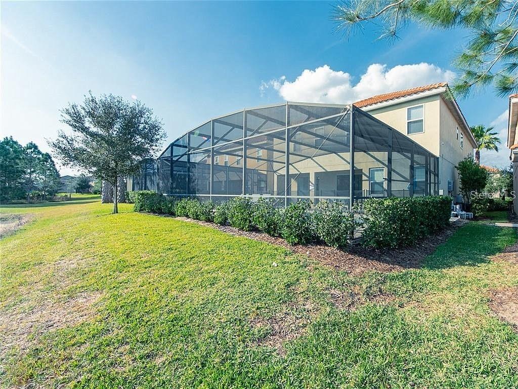 A backyard view of a house with a large screened-in pool enclosure and landscaping — 4357 ACORN COURT, DAVENPORT, FL