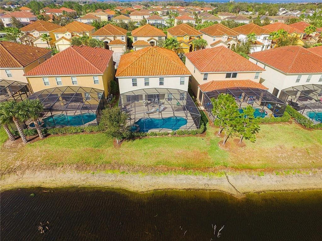 An aerial view shows three houses with screened-in pools and tile roofs facing a lake — 4357 ACORN COURT, DAVENPORT, FL