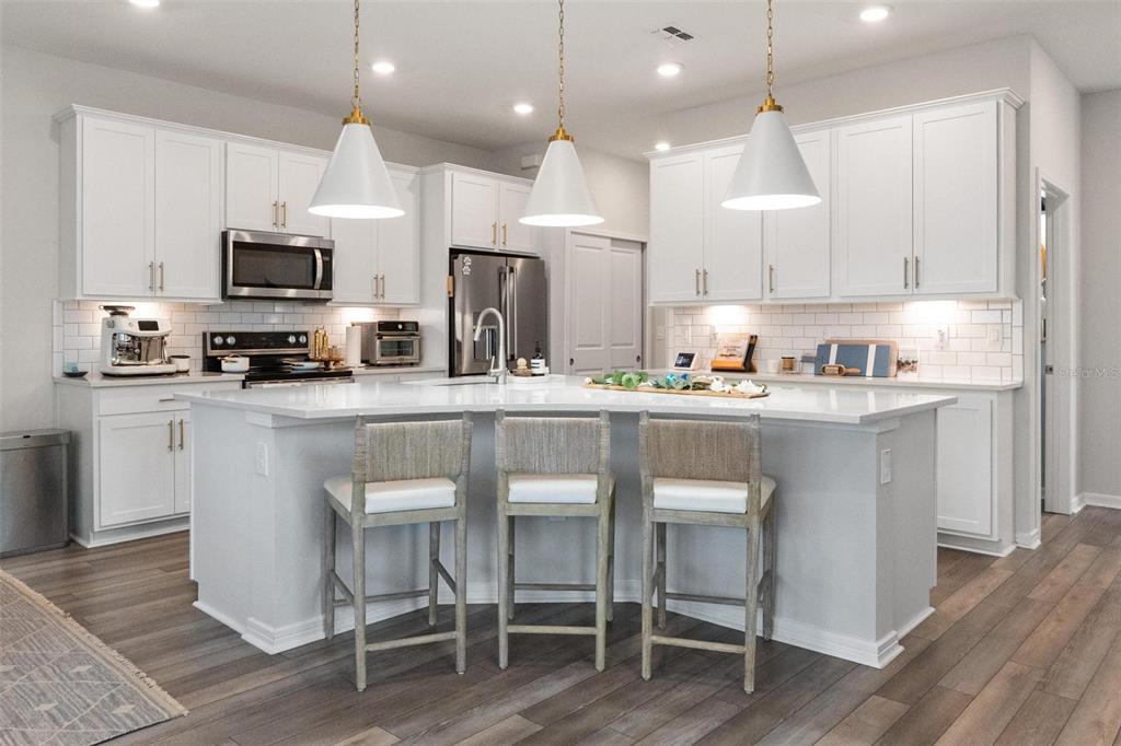 A modern kitchen features white cabinetry, a large central island with bar stools, and pendant lighting — 351 SURFSIDE AVENUE NE, ST PETERSBURG, FL