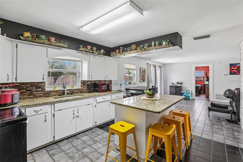 A kitchen with white cabinets, granite countertops, a central island, and yellow metal stools — 3435 SWINDELL ROAD, LAKELAND, FL
