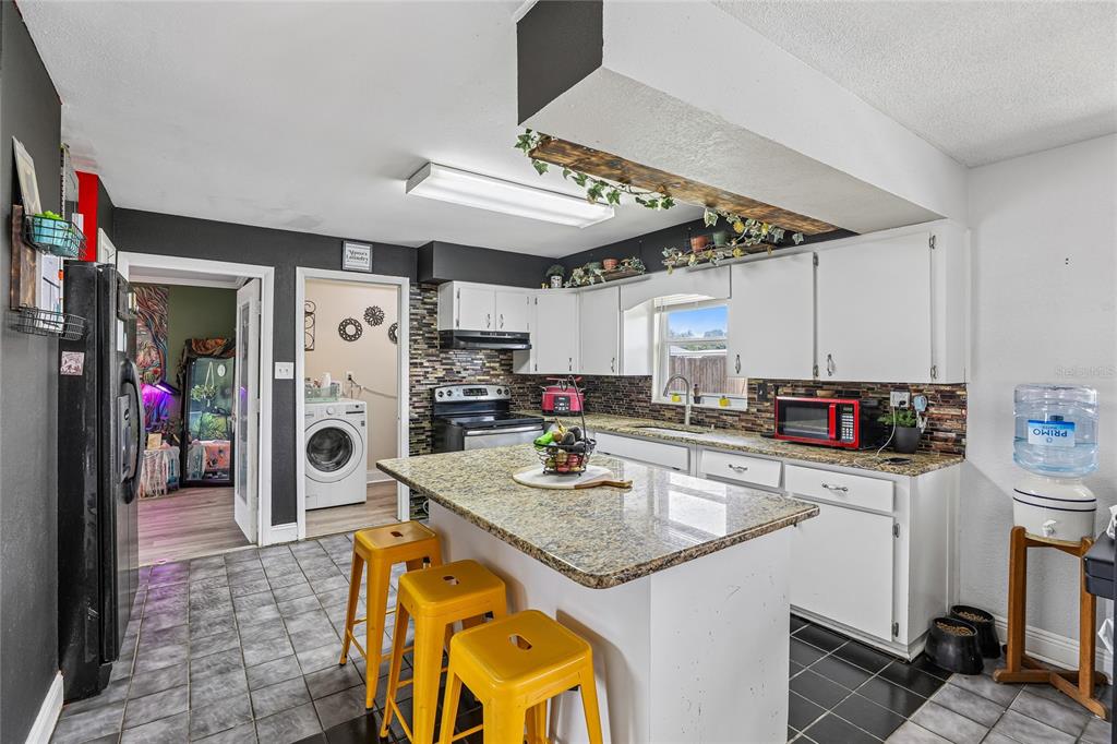 A kitchen features a granite-topped island, yellow stools, white cabinets, and dark tile flooring — 3435 SWINDELL ROAD, LAKELAND, FL